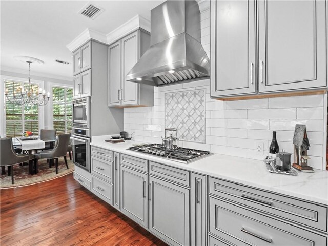 kitchen featuring tasteful backsplash, crown molding, wall chimney exhaust hood, appliances with stainless steel finishes, and dark wood-type flooring