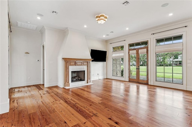 unfurnished living room featuring crown molding, light wood-type flooring, a fireplace, and french doors