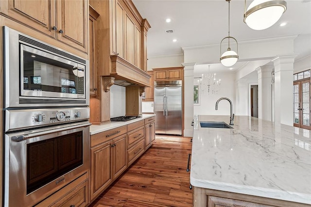 kitchen featuring ornate columns, decorative light fixtures, sink, a large island, and built in appliances