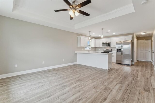 kitchen featuring light wood-type flooring, white cabinetry, ceiling fan, a tray ceiling, and appliances with stainless steel finishes