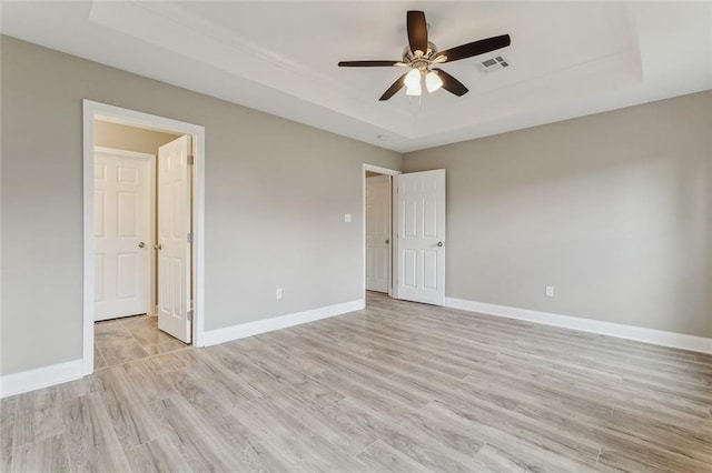 unfurnished room with light wood finished floors, a raised ceiling, visible vents, ceiling fan, and baseboards