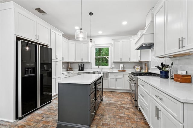 kitchen with white cabinetry, decorative backsplash, black fridge, custom range hood, and high end stainless steel range