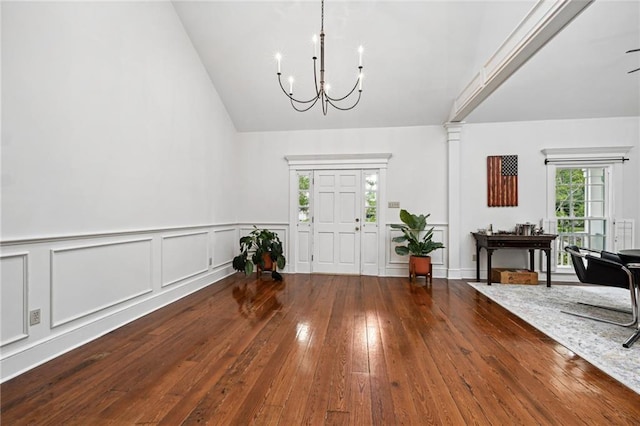 entryway with decorative columns, a chandelier, wood-type flooring, and vaulted ceiling