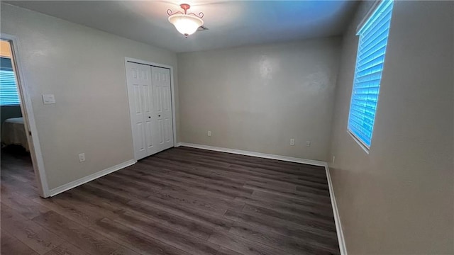 unfurnished bedroom featuring dark wood-type flooring, a closet, and baseboards