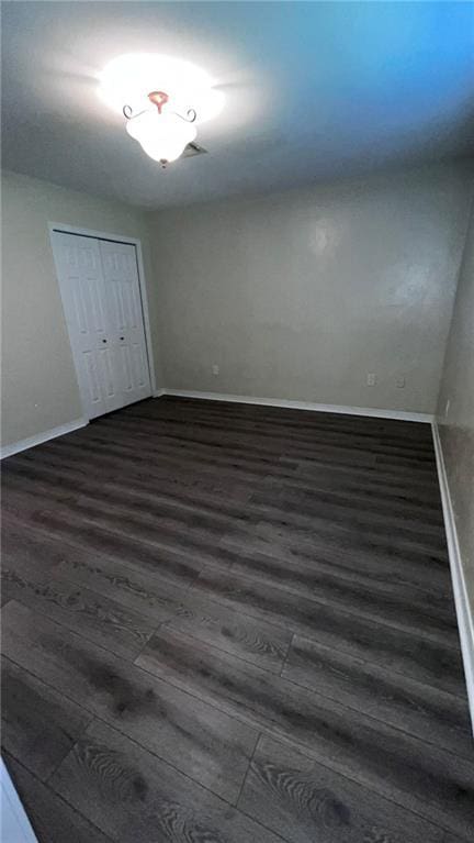 unfurnished bedroom featuring a closet, baseboards, and dark wood-style flooring