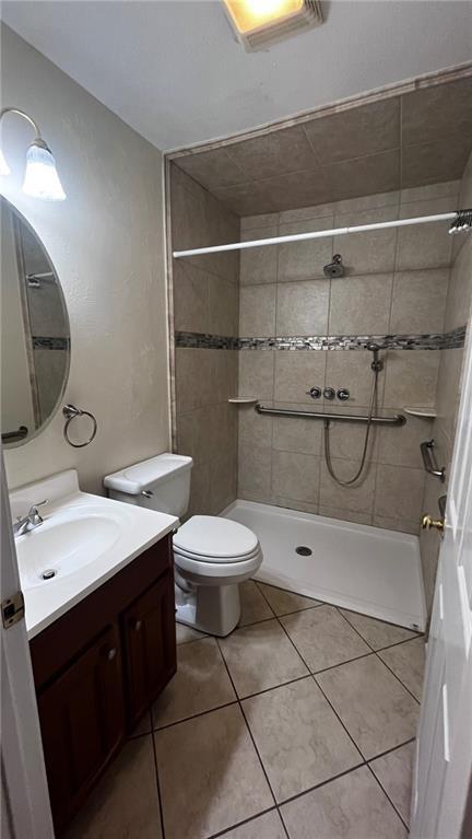 bathroom with toilet, tiled shower, tile patterned flooring, and vanity