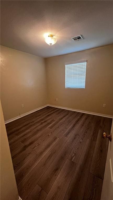 spare room featuring baseboards, visible vents, and dark wood finished floors