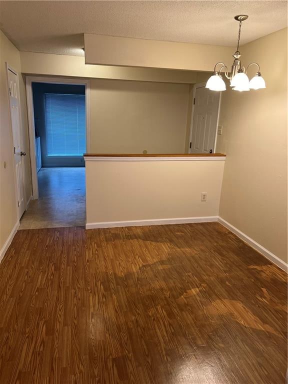 unfurnished room with an inviting chandelier, dark hardwood / wood-style floors, and a textured ceiling