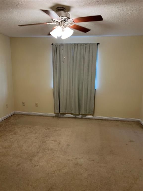 spare room with a textured ceiling, light colored carpet, and ceiling fan