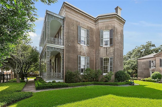 2027 Carondelet St, New Orleans, LA 70130 - rear view of house with a balcony, a lawn, a chimney, and stucco siding