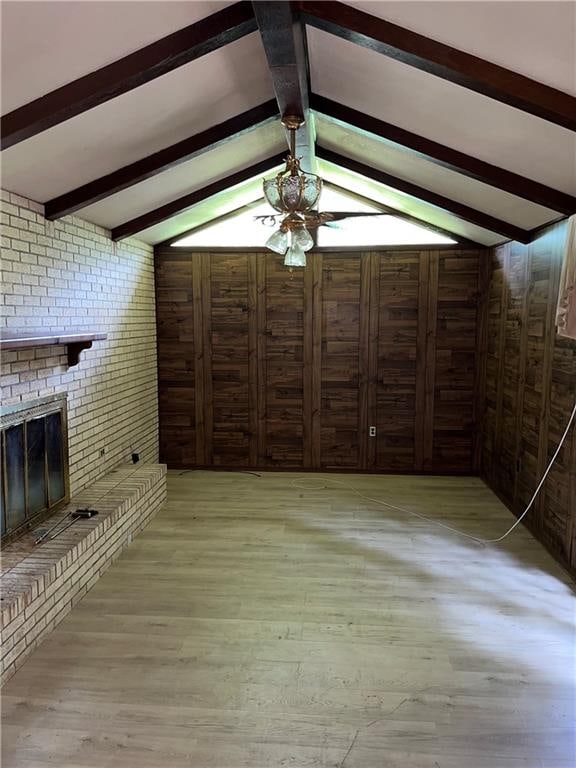 unfurnished living room featuring brick wall, a fireplace, ceiling fan, and wood walls