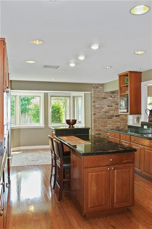 kitchen with a kitchen island, light hardwood / wood-style flooring, stainless steel microwave, and dark stone countertops