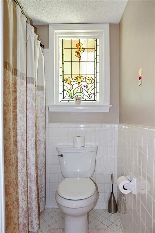 bathroom featuring toilet, a textured ceiling, tile patterned flooring, and tile walls