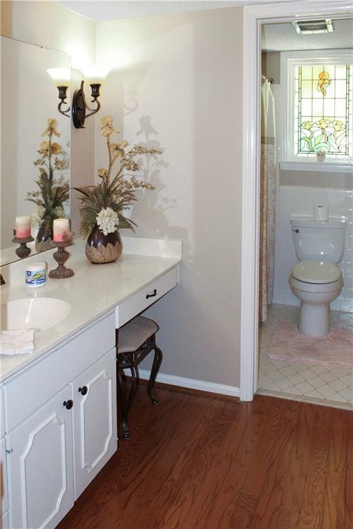 bathroom with hardwood / wood-style flooring, toilet, vanity, curtained shower, and tile walls