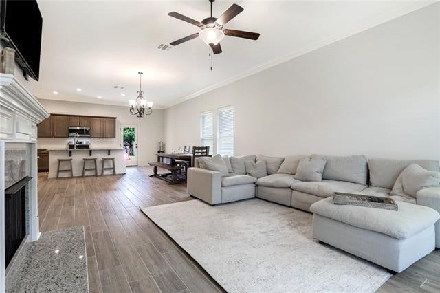 living room featuring ceiling fan with notable chandelier, a premium fireplace, ornamental molding, and hardwood / wood-style flooring