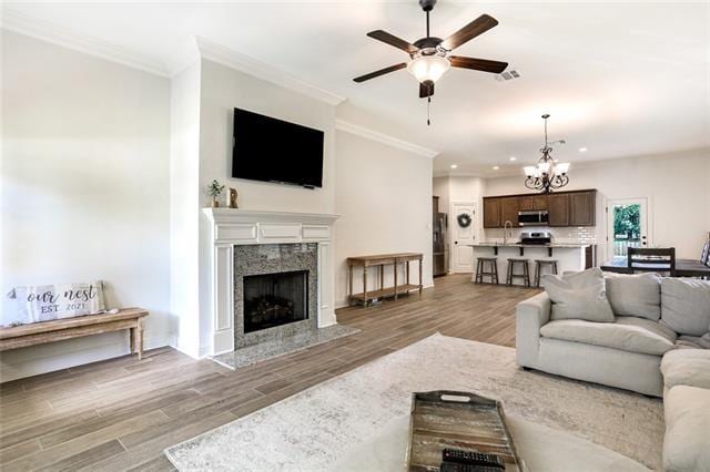 living room with light hardwood / wood-style flooring, a premium fireplace, crown molding, and ceiling fan with notable chandelier