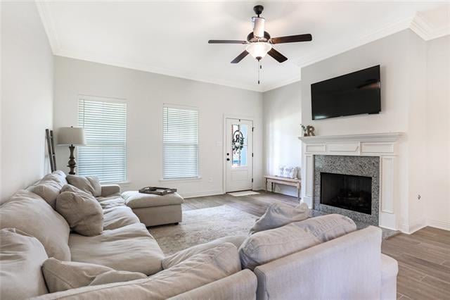 living room featuring ceiling fan, crown molding, light hardwood / wood-style flooring, and a high end fireplace