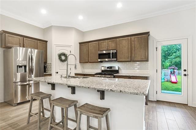 kitchen with stainless steel appliances, a kitchen island with sink, a healthy amount of sunlight, tasteful backsplash, and sink