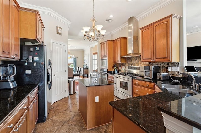 kitchen with sink, wall chimney exhaust hood, decorative light fixtures, a kitchen island, and appliances with stainless steel finishes