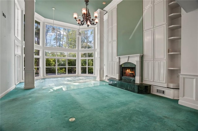 unfurnished living room with built in features, carpet flooring, a premium fireplace, a high ceiling, and an inviting chandelier