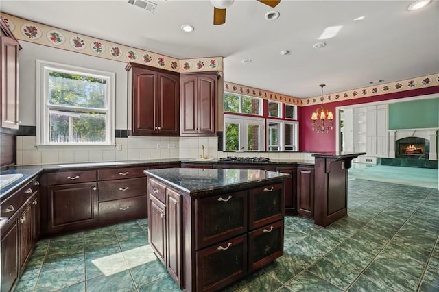 kitchen featuring ceiling fan with notable chandelier, backsplash, decorative light fixtures, and a kitchen island