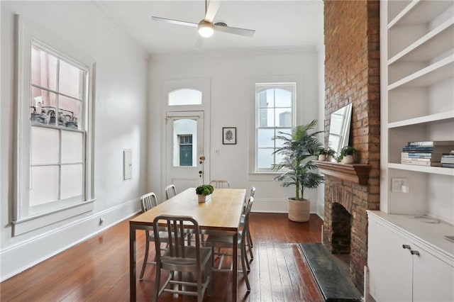 dining room with dark hardwood / wood-style floors, a large fireplace, ornamental molding, and ceiling fan