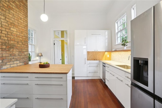 kitchen featuring dark hardwood / wood-style flooring, tasteful backsplash, stainless steel appliances, pendant lighting, and white cabinets