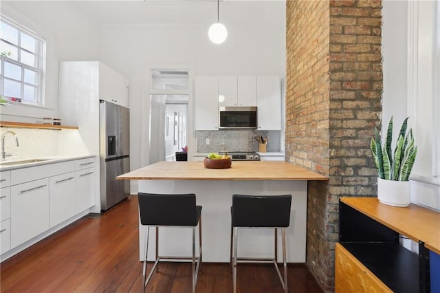 kitchen with decorative light fixtures, stainless steel appliances, white cabinetry, and sink