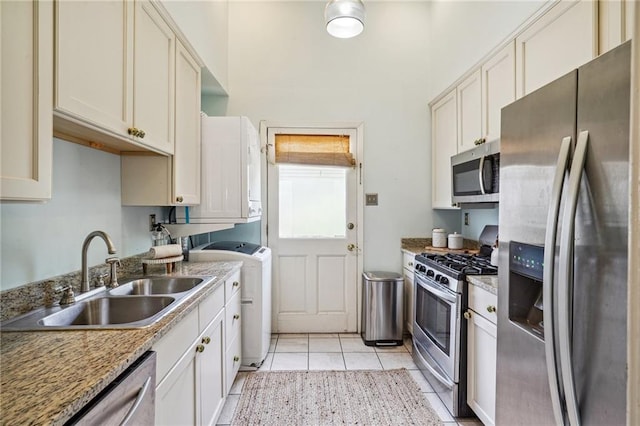 kitchen with light tile patterned flooring, sink, washer and dryer, light stone countertops, and appliances with stainless steel finishes