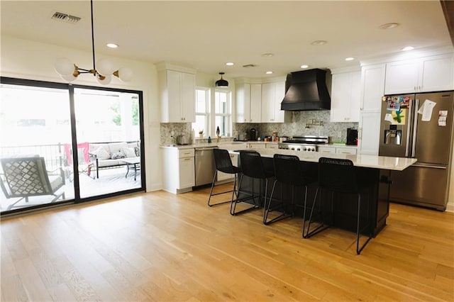 kitchen with white cabinetry, stainless steel appliances, a breakfast bar, and custom exhaust hood