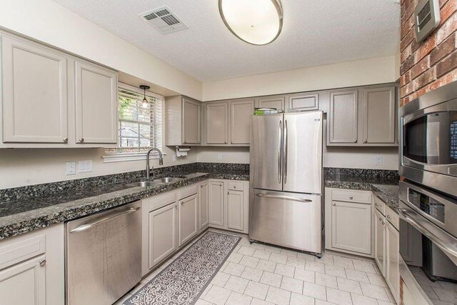 3412 Tolmas Dr, Metairie, LA 70002 - kitchen featuring stainless steel appliances, a sink, gray cabinetry, a textured ceiling, and dark stone counters