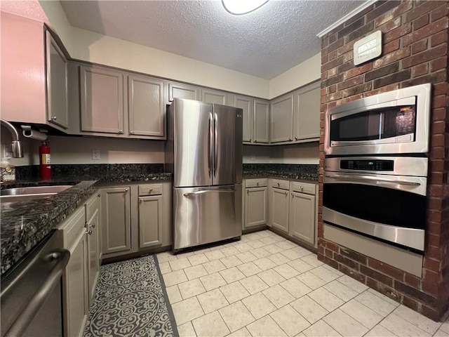 kitchen featuring sink, gray cabinets, appliances with stainless steel finishes, dark stone countertops, and a textured ceiling