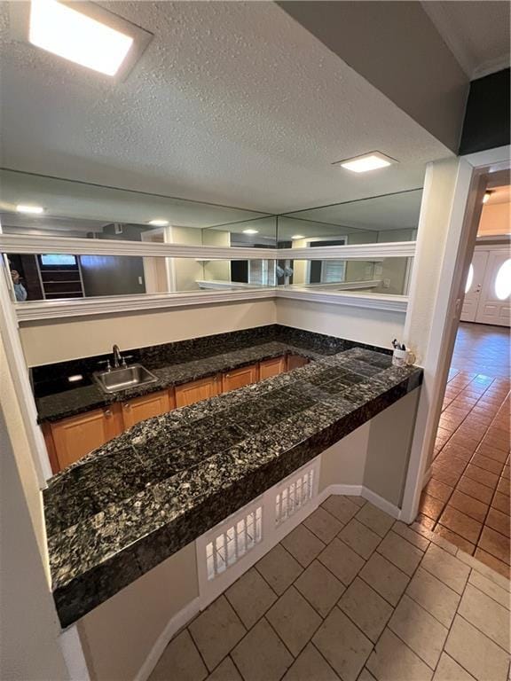 bar with sink, tile patterned floors, a textured ceiling, and dark stone counters