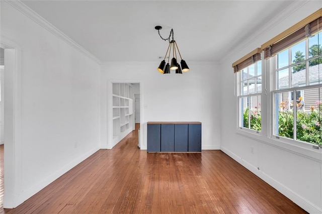 unfurnished dining area featuring dark wood-type flooring, crown molding, and a notable chandelier