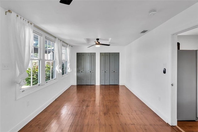 unfurnished bedroom with multiple closets, ceiling fan, wood-type flooring, and stainless steel fridge