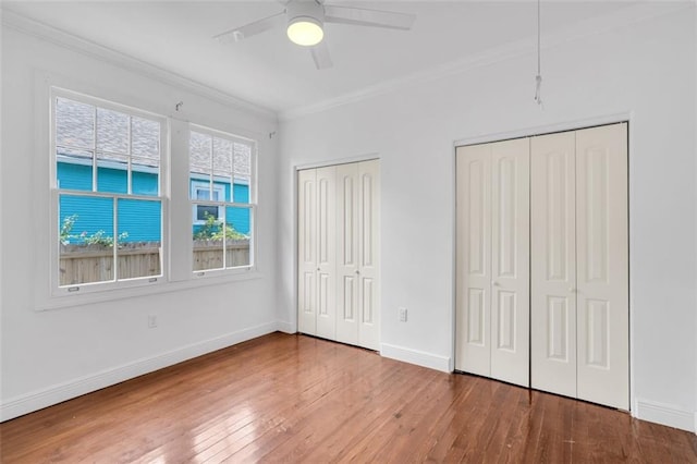 unfurnished bedroom with multiple closets, ornamental molding, hardwood / wood-style floors, and ceiling fan