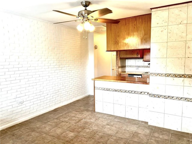 kitchen featuring brick wall, kitchen peninsula, dark tile patterned floors, and ceiling fan