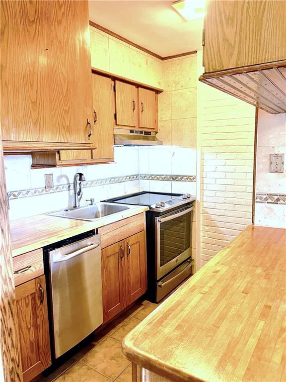 kitchen featuring a sink, light tile patterned floors, under cabinet range hood, stainless steel appliances, and butcher block countertops