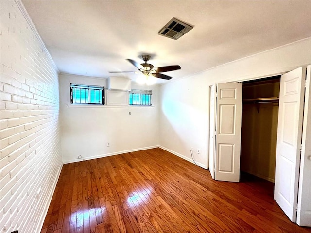 unfurnished bedroom with wood-type flooring, a closet, crown molding, ceiling fan, and brick wall