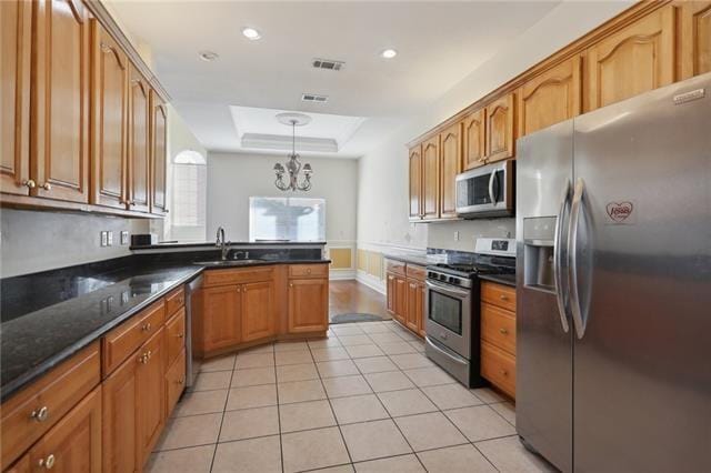 kitchen featuring stainless steel appliances, sink, hanging light fixtures, a tray ceiling, and a notable chandelier