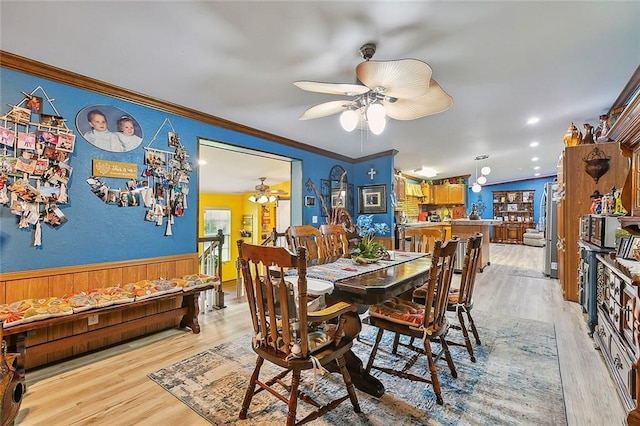 dining room with ornamental molding, ceiling fan, light hardwood / wood-style floors, and wood walls