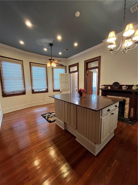 kitchen with dark wood-type flooring, crown molding, decorative light fixtures, a kitchen island, and white cabinetry