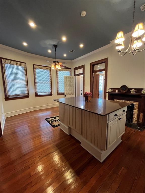 kitchen with pendant lighting, white cabinets, dark hardwood / wood-style floors, ornamental molding, and a kitchen island