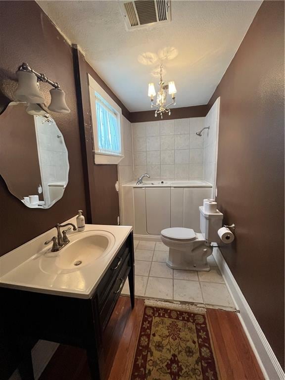 bathroom with a tub to relax in, vanity, a notable chandelier, hardwood / wood-style floors, and toilet