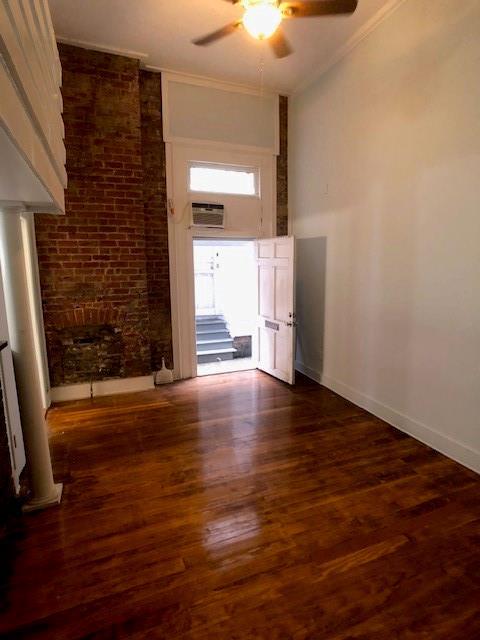 empty room with crown molding, ceiling fan, brick wall, and dark hardwood / wood-style flooring