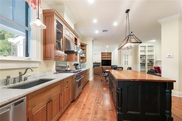 kitchen with appliances with stainless steel finishes, light hardwood / wood-style flooring, wood counters, a kitchen island, and wall chimney exhaust hood