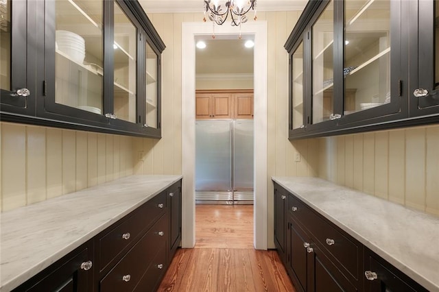 bar featuring light stone countertops, light hardwood / wood-style flooring, a chandelier, and ornamental molding