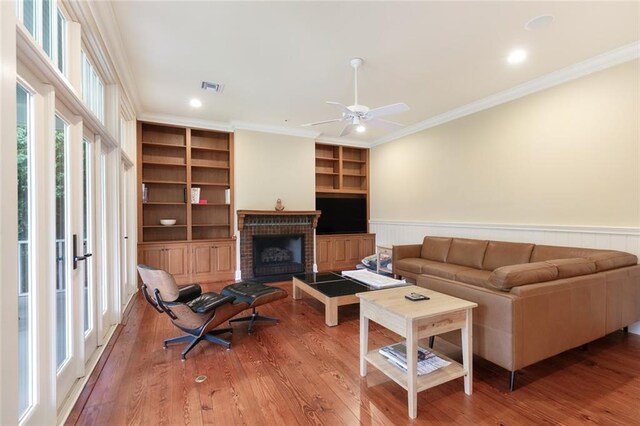 living room with built in features, ceiling fan, light hardwood / wood-style floors, a fireplace, and ornamental molding