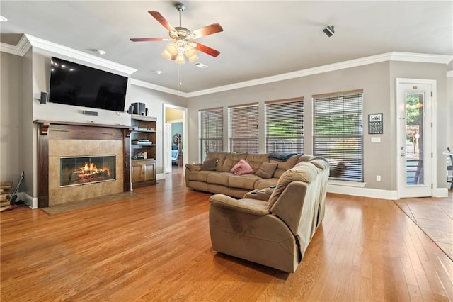 living room with a fireplace, crown molding, light wood-type flooring, and ceiling fan