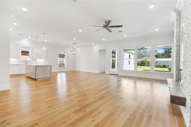 unfurnished living room with sink, ceiling fan with notable chandelier, a stone fireplace, and light hardwood / wood-style floors